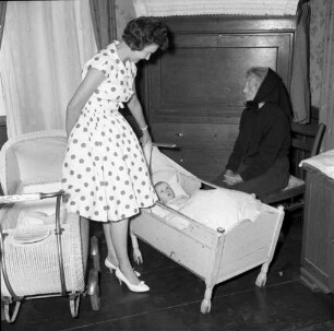 Eine Frau an einem Kinderbett, wohl in einem Museum