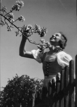 Junges Mädchen mit blühendem Zweig hinter einem Gartenzaun