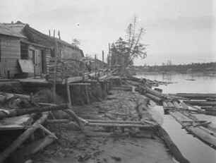 Saisonsiedlung am Horonai-gawa (Poronai) : Blockhütten und Holzreste am Flussufer