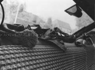 Heckablage eines Ford Fiestas mit dort abgelegten Kleidungsstücken sowie unscharfer Ausblick durch die Heckscheibe auf ein Wohnhäuser(Foto Altersgruppe 18-21)