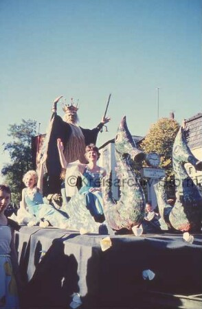 Reinfeld: Karpfenfest: Umzug: Paul-von-Schoenaich-Straße: Motto-Wagen mit Neptun, Nymphen und Seepferdchen: hinten Handelsbank in Lübeck mit Uhr: davor Zuschauer: hinten links Fahnenmasten und Bäume: 11. Oktober 1959