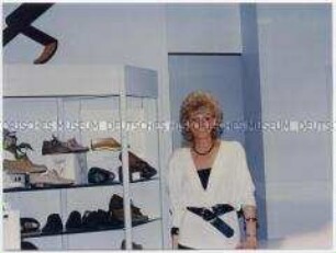 Schuhverkäuferin neben Schuhregal (Altersgruppe 18-21)