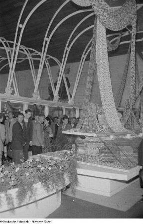 Besucher der Herbstmesse 1953 an einer Glasvitrine mit Stoffbahnen sowie Stoffballen