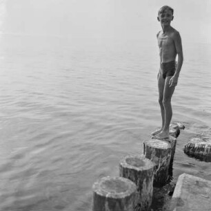 Junge steht auf einem Wellenbrecher vor dem offenen Meer
