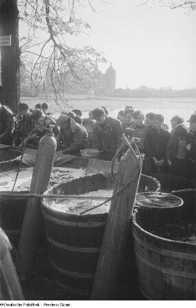 Wasserbehälter zur Aufbewahrung des gefangenen Fisches umlagert von Fischern und Kindern, im Hintergrund das Moritzburger Schloß