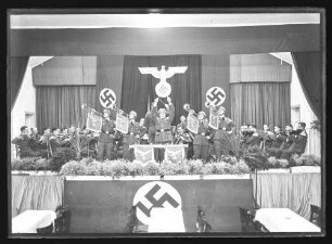 Musikkapelle mit vier Fanfarenspieler und Dirigent (im Hintergrund Reichsadler)