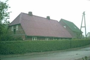 Fachwerkkate: Giebelseite, traufständige Straßenseite mit Eingangstür: davor Hecke, Straße