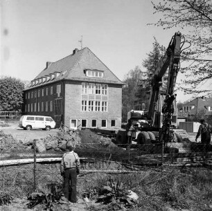 Woldenhorn-Schule: Sonderschule des Kreises Stormarn für geistig behinderte Kinder: Ecke Reeshoop / Schulstraße: Erweiterungsbau: in Bau: Bagger bei Ausheben der Baugrube: Arbeiter, Aushub, Eisenträger, Bretter, Bauwagen, Kleintransporter: hinten Altbau: Blick von Hans-Schadendorff-Stieg aus: im Vordergrund Kind bei Blick durch Maschendrahtzaun