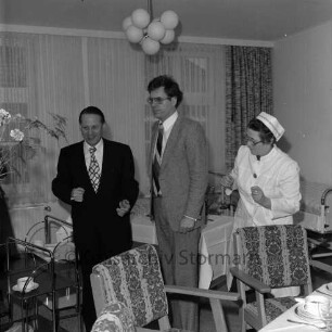 Evangelische Kirchengemeinde: Predigerwitwenhaus: am Neuhöfer Teich, Ecke Lokfelder Damm: Feier: Pastor Werner Arnold, Mann, Gemeindeschwester: zwei Servierwagen, Blumenstrauß: hinten Tisch mit Geschirr und Kuchen, Krankenbett: im Vordergrund gedeckter Kaffeetisch