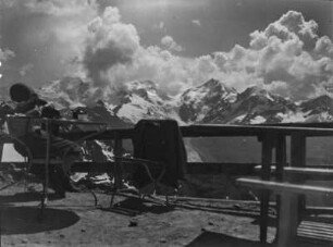 An der Hütte : Ein Bergsteiger sitzt auf der Terrasse von der die Berninagruppe überblickt werden kann.
