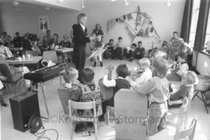 "Alte Schule": Familien-Frühlingsfest: Montessori-Spielkreis bei Musikvortrag: rechts Kinder mit Instrumenten auf Stühlen: in der Mitte Leiterin Brigitte Peters: links Kinder und Erwachsene an Tischen