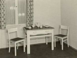 Küchentisch mit ausziehbarer Spüle und zwei Küchenstühle : Leipzig-Zentrum. Messehaus "Union", Richard-Wagner-Straße 10/11. Küchentisch mit ausziehbarer Spüle und zwei Küchenstühle. Holz, weiß lackiert (1956; VEB Wittstocker Holzindustrie) in Ausstellungskoje