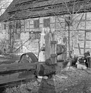 Drahtmühle: Restaurierung: vorn Mühlenwerk der Papiermühle mit Holzbohlen: dahinter Bäume: rechts Stapel mit Holzstücken