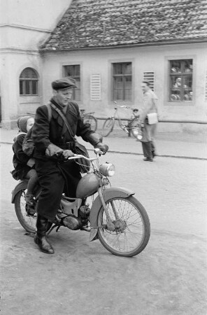 Mann fährt mit einem Moped, auf dem Rücksitz ein kleines Mädchen