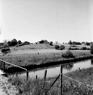 Klein Barnitz: Trave: dahinter Knicklandschaft und Klein Barnitz: vorn links Brückengeländer der Fußgängerbrücke: rechts Zaun