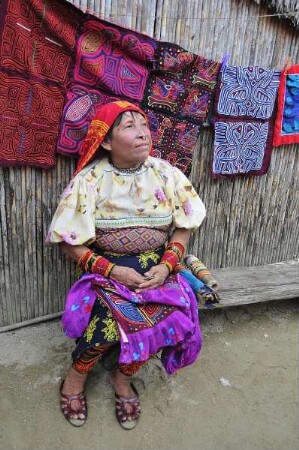 Kuna Yala - Kuna-Indianerin mit Mola Kunstwerken : Eine Kuna-Indianerin sitzt vor ihrer Wohnhütte, im Hintergrund sind ihre selbstgefertigten textilen Mola-Kunstwerke zu sehen. Aufgenommen am 12. September 2011 auf einer der San Blas Inseln im autonomen Gebiet der Kuna-Indianer vor der Atlantikküste der Republik Panama
