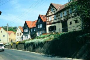 Dorfstraße mit Böschungsmauer, darüber Häuserzeile, Ensemble vorwiegend giebelständiger Häuser