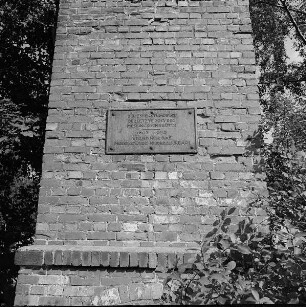 Rodewisch, Lengenfelder Straße. Schornsteinstumpf eines ehemaligen Messingwerkes (Ziegelstein; um 1860), Teilansicht mit Gedenktafel (signiert und datiert K. Schott 1962) mit Inschrift "Der Essenstumpf ist der letzte Rest der Messingbrennhütte. 1603-1924 stand hier das Messingwerk Niederauerbach"