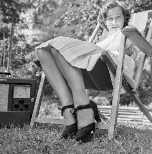 Elisabeth Gremmler sitzt in einem Klappstuhl im Garten, neben ihr steht ein Rundfunkempfänger