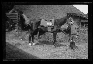 Pferdebursche mit Pferd vor einer reetgedeckten Art Scheune