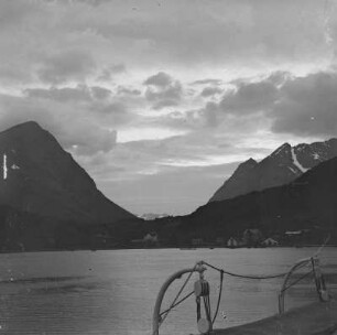 Norwegen. Blick von einem Passagierdampfer über einen Fjord gegen Ortschaft mit Fischereihafen vor Steilküste