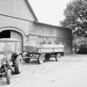 Landwirtschaft: links Trecker und Anhänger mit Jauchetanks: dahinter Scheune: hinten rechts Bäume