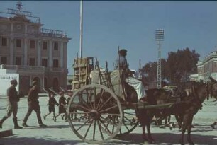 Reisefotos Spanien. Straßenbild mit Soldaten, uniformierten Jungen und Pferdefuhrwerk. Im Hintergrund öffentliches Gebäude mit Metallettern "Franco" auf der Dachkante