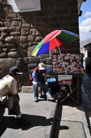 Cusco - Sonnenschirm vor einer Inka-Mauer : Unter einem Sonnenschirm vor einer Mauer aus der Inka-Zeit bietet ein Mann Zigaretten an. Aufgenommen am 30. August 2011 in der einstigen Inka-Hauptstadt Cusco