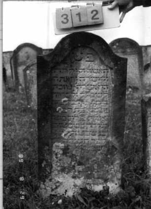 Grabstein 312 (Index: 100107726) Material: grauer Sandstein Zustand: sehr stark verwittert, teilweiser Textverlust Maße HxBxT: 107x50x11 cm Beschreibung: Stele, geschwungener Bogenabschluß, Schriftfeld eingetieft: Grabstein 312