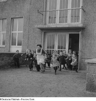 Kindergärtnerin mit Kindern vor dem Kindergartengebäude