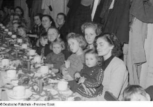 Kinder und Mütter an einer gedeckten und geschmückten Tafel bei der Weihnachtsfeier des Verlags Volk und Wissen