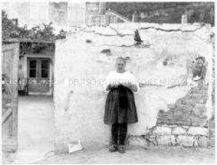 Strickende Frau an eine Hauswand gelehnt