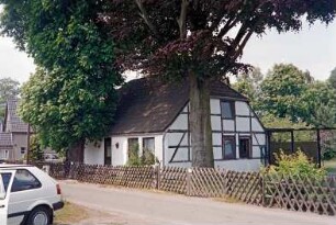 Horst (2): traufständige Fachwerkkate: Straßenfront mit Eingangstür: Giebelseite Wohntrakt: davor zwei Bäume, Jägerzaun: rechts Garten