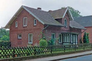 Hoisdorfer Weg 2: traufständiges Wohnhaus aus Backstein: Straßenfront mit Zwerchhaus, mittigem Eingangsvorbau: Giebelseite: vorne Jägerzaun