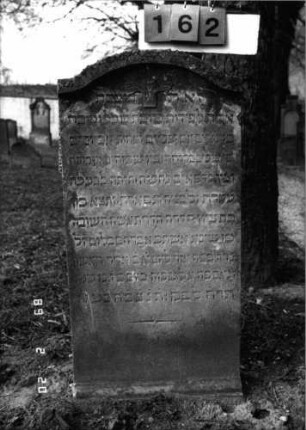 Grabstein 162 (Index: 99798648) Material: Sandstein Zustand: gut Maße HxBxT: 109x54x13 cm Beschreibung: Stele mit flachem Sattelbogenabschluß, kleiner Verdachung und seitlichen Quasten Symbolik: geflügelte Sanduhr: Grabstein 162