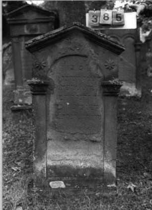 Grabstein 385 (Index: 99789426) Material: Sandstein Zustand: sehr stark verwittert mit Textverlust Maße HxBxT: 125x63x16 cm Symbolik: achtzackige Sterne Besonderheit: Stele fast identisch mit Nr. 388: Grabstein 385