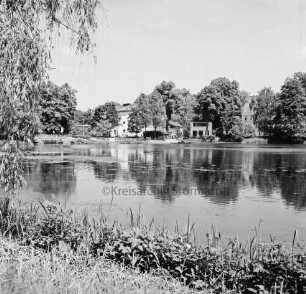 Mühlenteich: Blick von Süden Am Mühlenteich auf gegenüberliegendes Ufer: hinten Mitte zwischen Bäumen Elektriziätswerk Reinbek-Wentorf GmbH [später: e-werk Sachsenwald]: hinten rechts Schloss Reinbek: hinten links Brücke der Schlossstraße über Bille: vorn links Baum