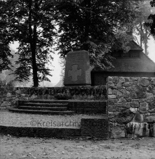 Rosenstraße / Dorfstraße: Ehrenmal mit Stufen und Feldsteinmauer: dahinter Bäume und Haus