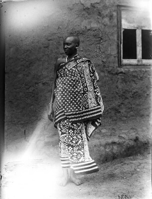 Frau der Massai : Portrait einer Frau der Massai in einem gemusterten Gewand vor einem Gebäude stehend.