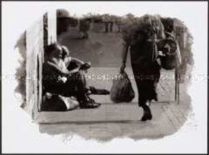 Zwei Obdachlose sitzen am Rand eines Bürgersteiges mit vorbeilaufender Passantin (Prämiertes Foto Sonderthema: Anders leben)