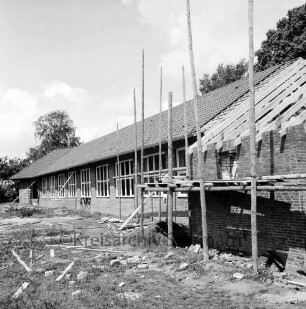 Volksschule: Schulkoppel: Neubau vor Fertigstellung: vorn rechts Turnhalle im Rohbau mit Gerüst: hinten Bäume: vorn Baumaterial