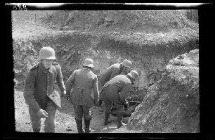 Übungsgelände II bei Mouzon (Dep. Ardennes, Frankreich): 4 Soldaten mit Stahlhelm in einem Graben neben einem mit einem Radkranz am Boden liegenden Kriegsgerät