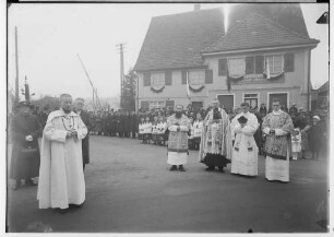 Primizfeier Ruf-Eisele in Sigmaringendorf 1936; Im Mittelpunkt Neupriester mit Eltern, dabei Geistlichkeit; im Hintergrund Zuschauer vor dem Haus Bäckerei-Konditorei Josef Aleker