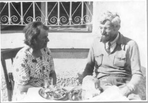 Hans und Etha Richter, im Freien vor einem vergitterten Fenster an einem Tisch sitzend