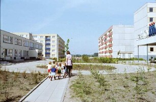 DDR. Kindergartengruppe in einem Neubeaugebiet auf einem Spaziergang. Rechts eine HO-Kaufhalle