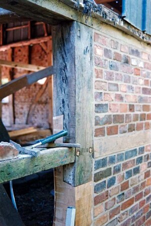 Dorfplatz (2): Fachwerkscheune: Sanierung: Detailaufnahme: Außenwand, Pfosten und Riegel nach teilweiser Erneuerung, vorne Gefache nach Entfernung von Ausmauerung, Blick in Innenraum, Werkzeug, oben Blechverkleidung: Juli 1994