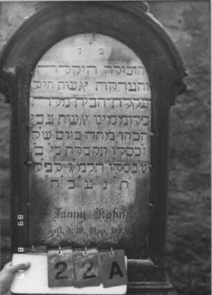 Grabstein 22 (Index: 100105740) Material: Sandstein und Marmor Zustand: Schrifttafel zerbrochen und repariert Maße HxBxT: 158x62x31 cm Beschreibung: Stele, profilierter Sockel, Rundbogenabschluß mit Aufsatz, eingesetzte Schrifttafel Steinmetz: Klein: Grabstein 22A
