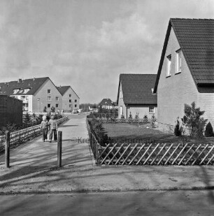 Neubausiedlung "Im Weeden": rechts Einfamilienhäuser mit Vorgarten und Jägerzaun: hinten links Wohnblocks: dazwischen Fußweg mit Kindern