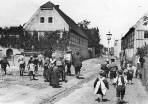 Coswig, Hauptstraße Ecke Ravensburger Platz. Straßenszene mit Musikanten (u. a. Trommler) und hinterherlaufender Kinderschar. Links Gehöft des Bauern Hantusch (Abriß 1937 wegen Straßenerweiterung), rechts Stellmacherei Ernst Grütze