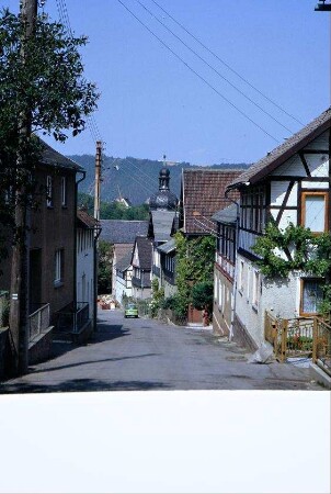 steile Dorfstraße, beidseitig Häuser, in der Mitte Kirchturmspitze